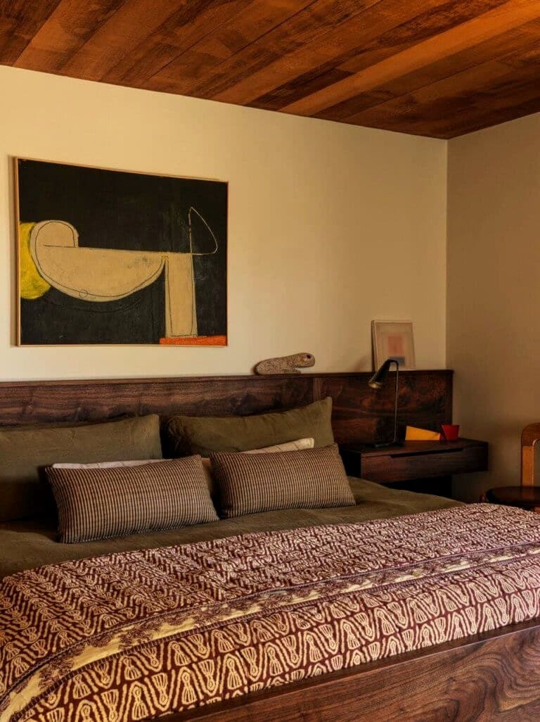 A warm bedroom with a slatted wood headboard and framed art